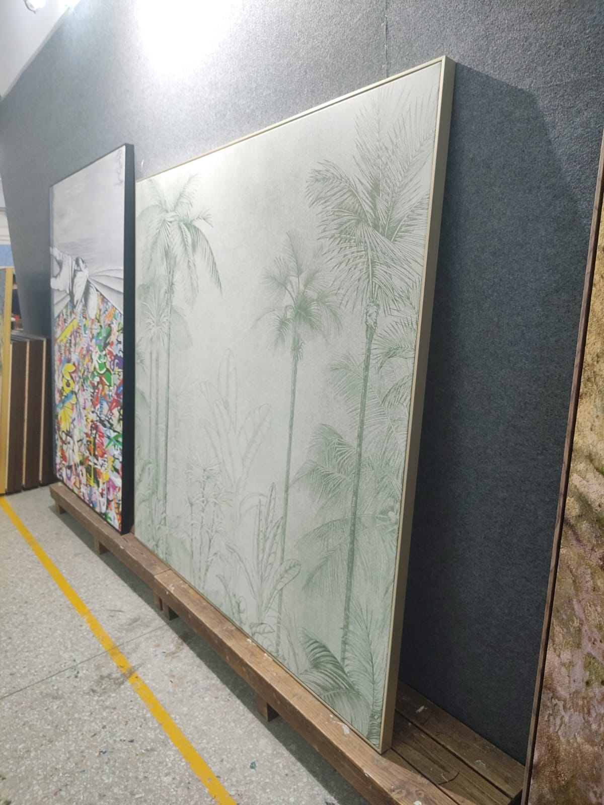A large artwork featuring palm trees, displayed against a gray wall in an art space