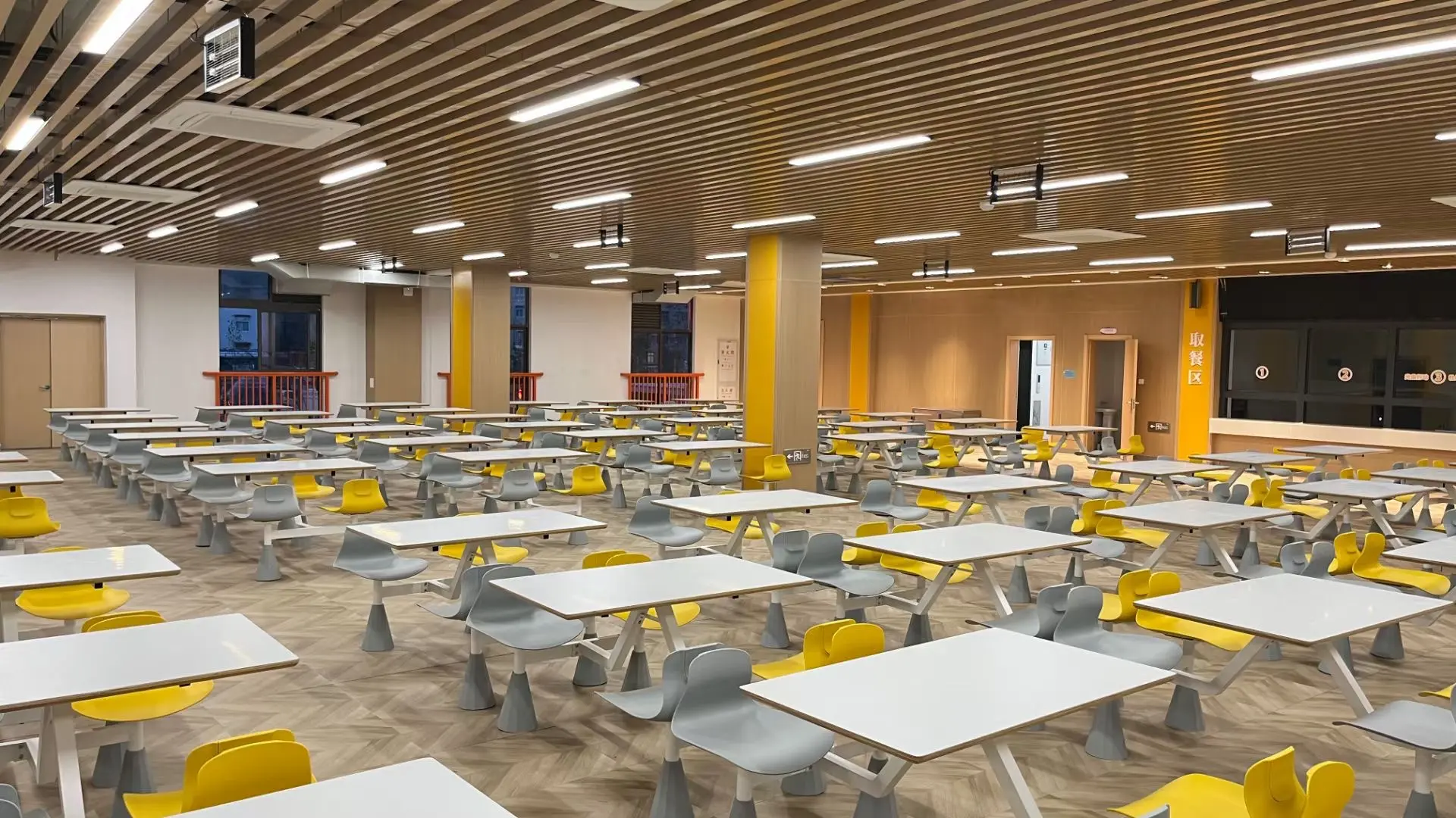 Spacious cafeteria with modern tables and colorful yellow chairs in a bright setting.