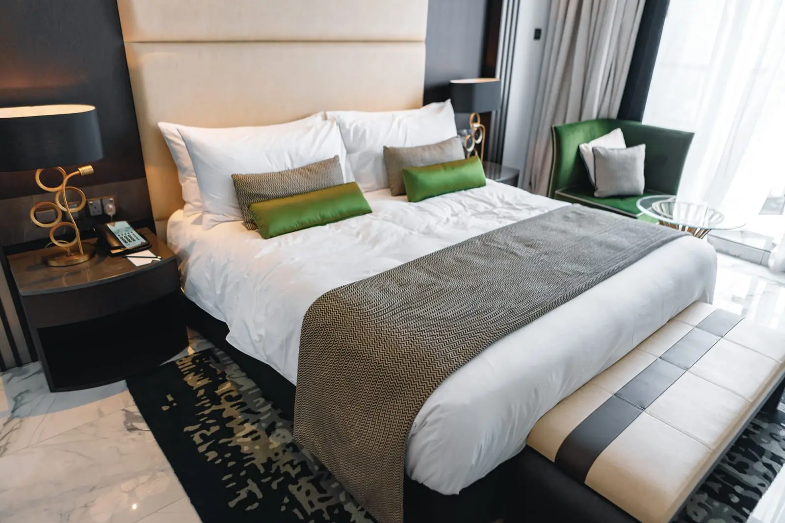 A luxurious hotel bed with white linens, green accent pillows, and stylish decor.