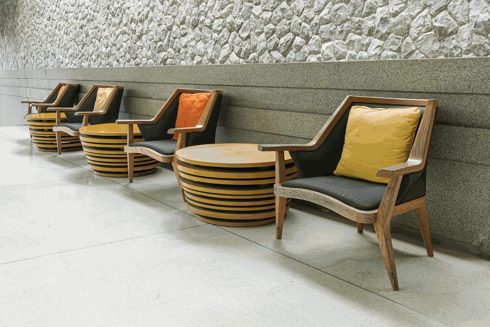 A modern seating arrangement for public areas featuring stylish wooden chairs with colorful cushions and a round wooden coffee table, ideal for hotel lobbies.
