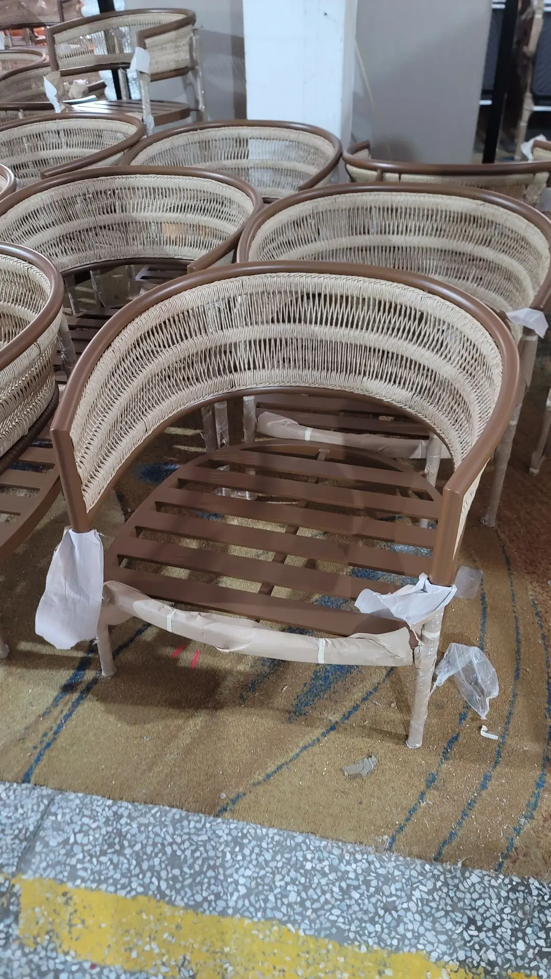 A collection of curved wicker chairs with wooden frames arranged in a warehouse.