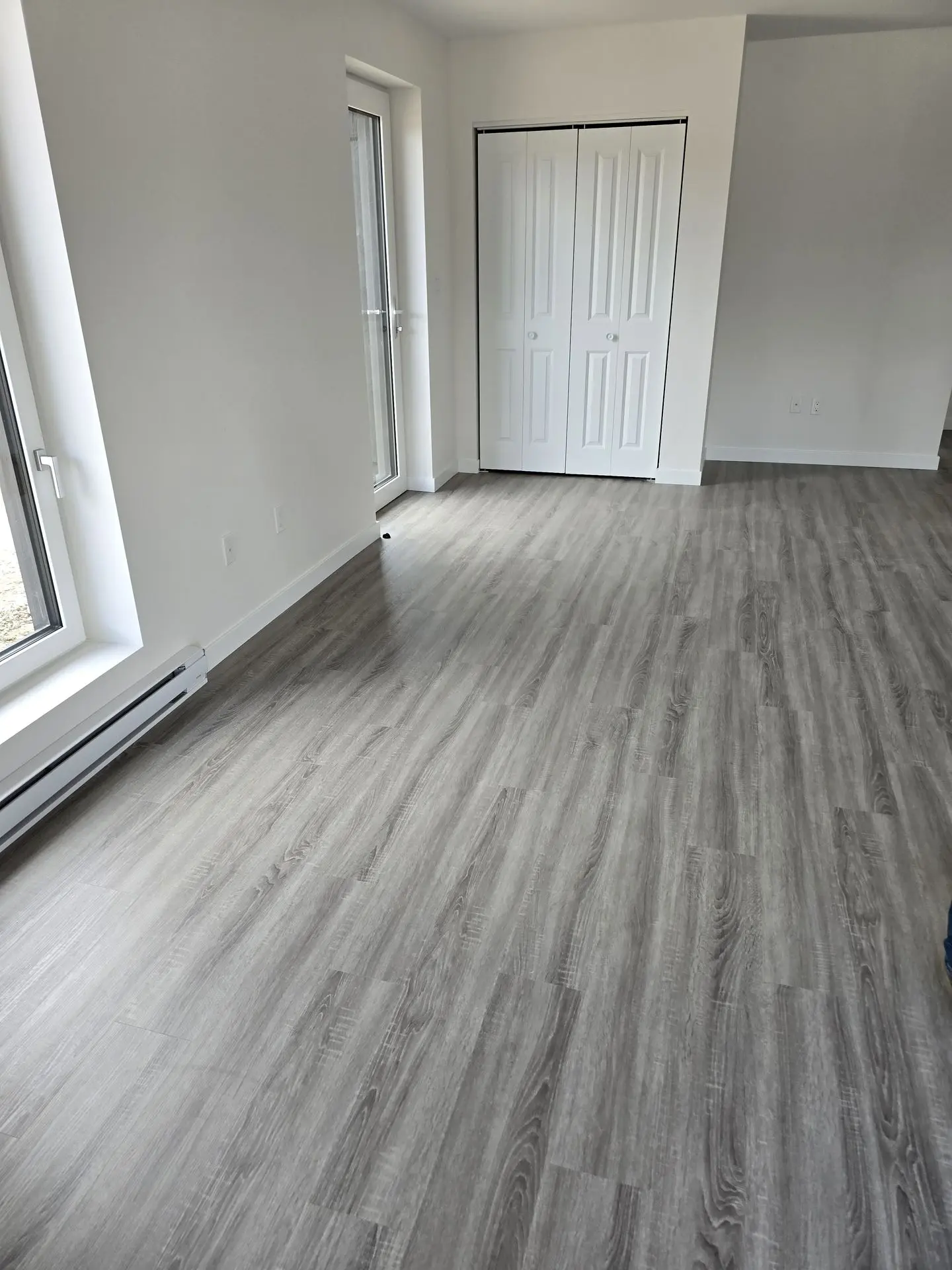 Interior view of a room featuring gray SPC (Stone Plastic Composite) flooring, large windows, and closet doors.