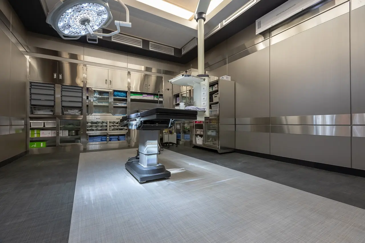 A modern surgical operating room equipped with a surgical table, overhead lights, and stainless steel cabinets filled with medical supplies.