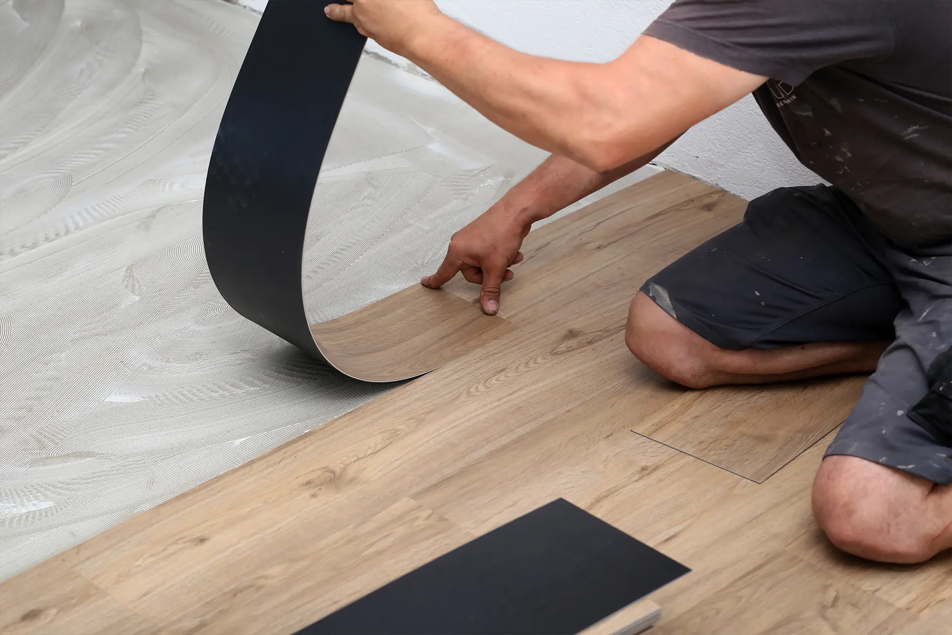 A person installing luxury vinyl tiles on a floor, carefully aligning a black tile with existing wood-patterned tiles.