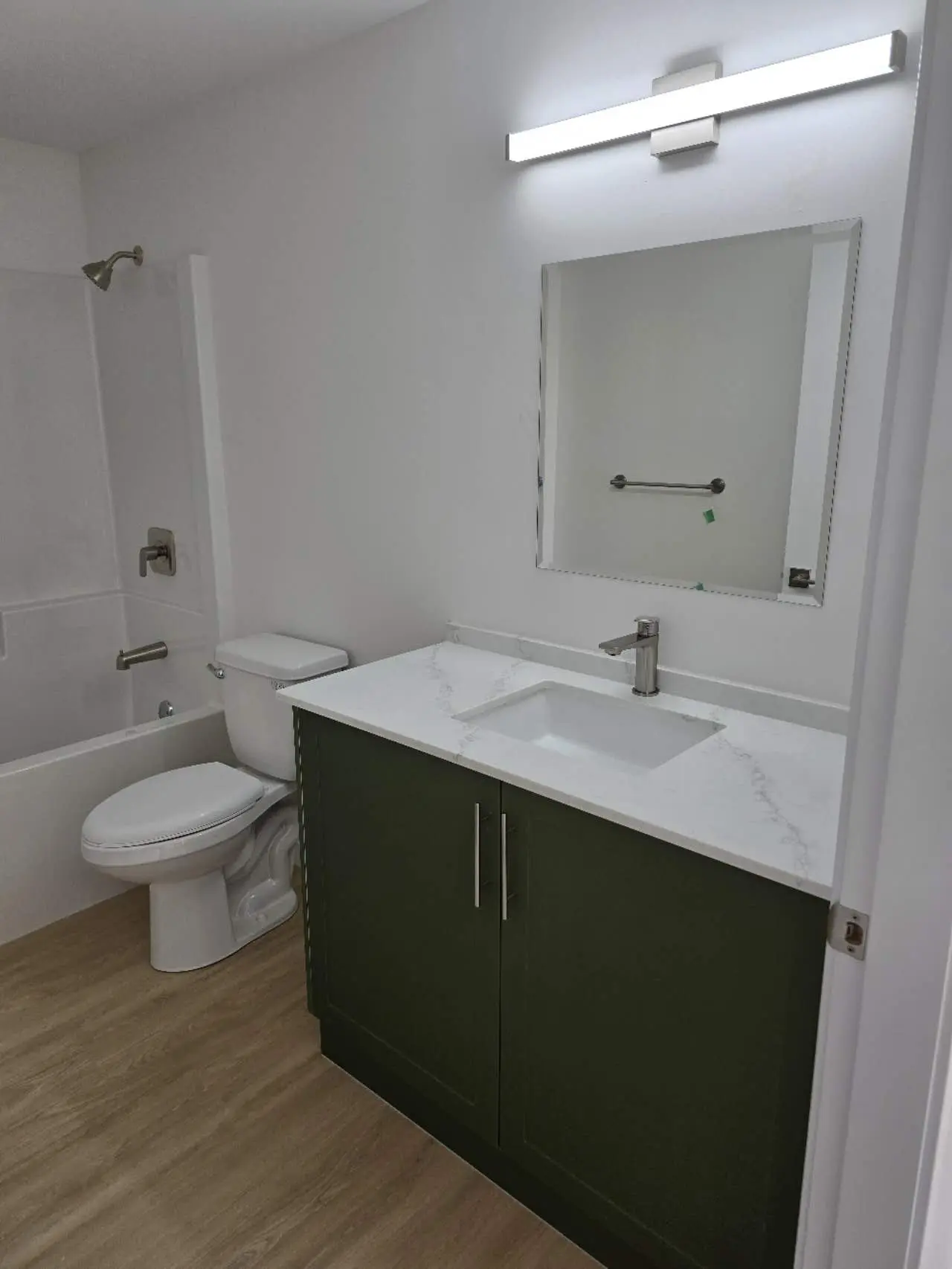 Modern bathroom featuring a green vanity with a marble countertop, a large mirror, and a bathtub.