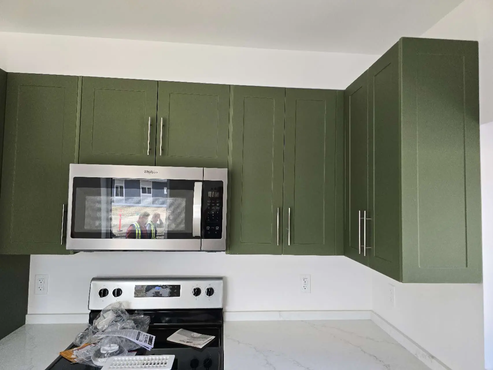 Modern kitchen featuring green cabinetry, a stainless steel microwave, and a sleek black stove.