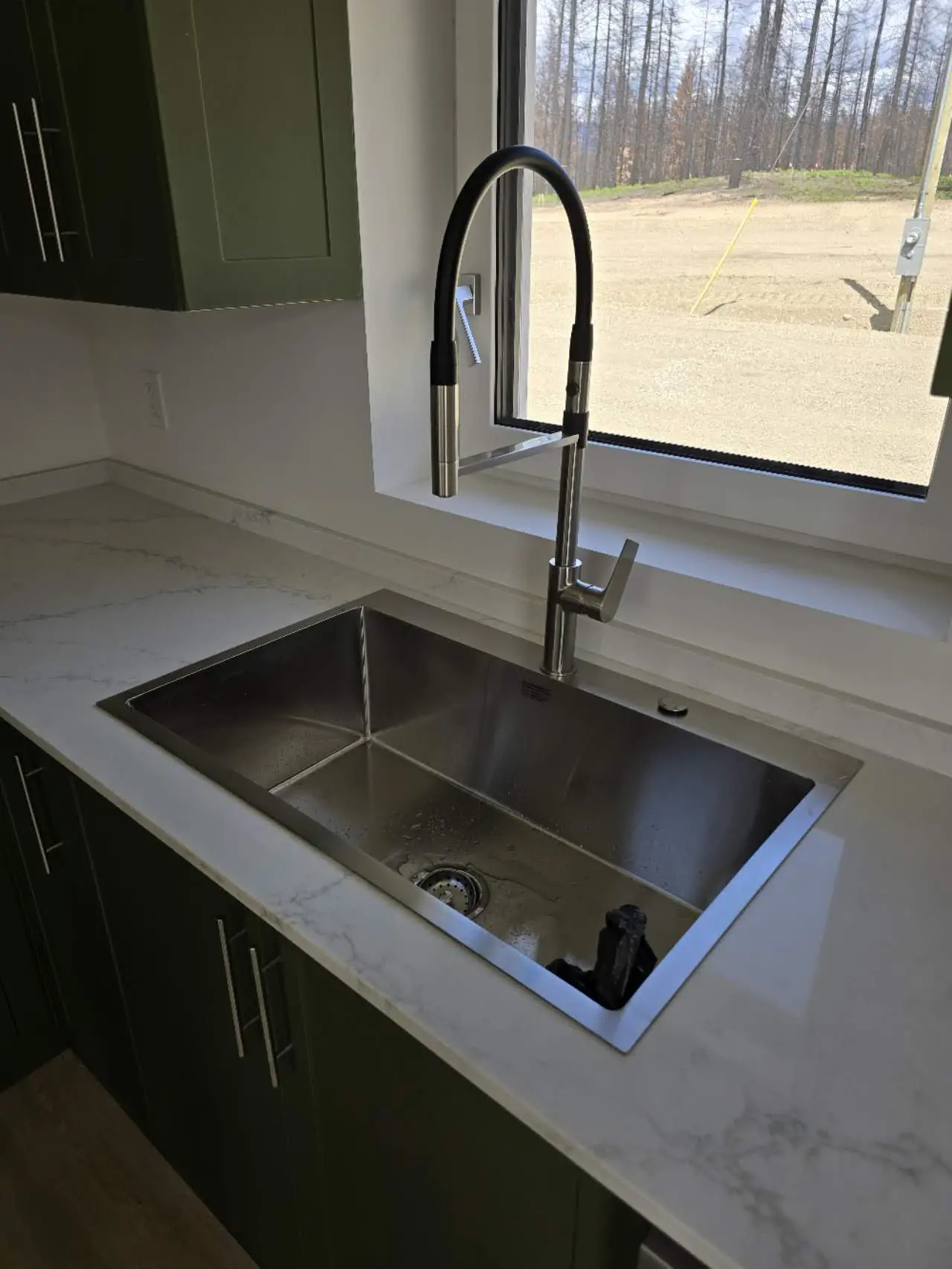 Close-up view of a modern kitchen sink with a sleek faucet, surrounded by green cabinetry and a marble