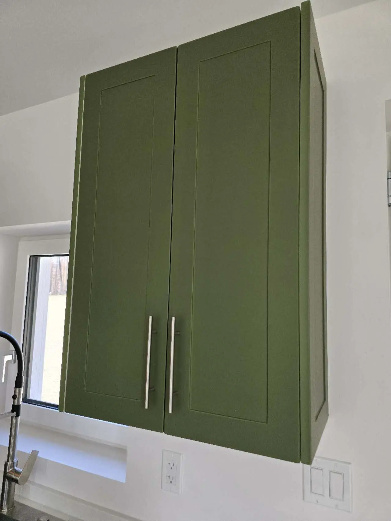 Close-up of green kitchen cabinets with sleek handles, featuring modern design elements.