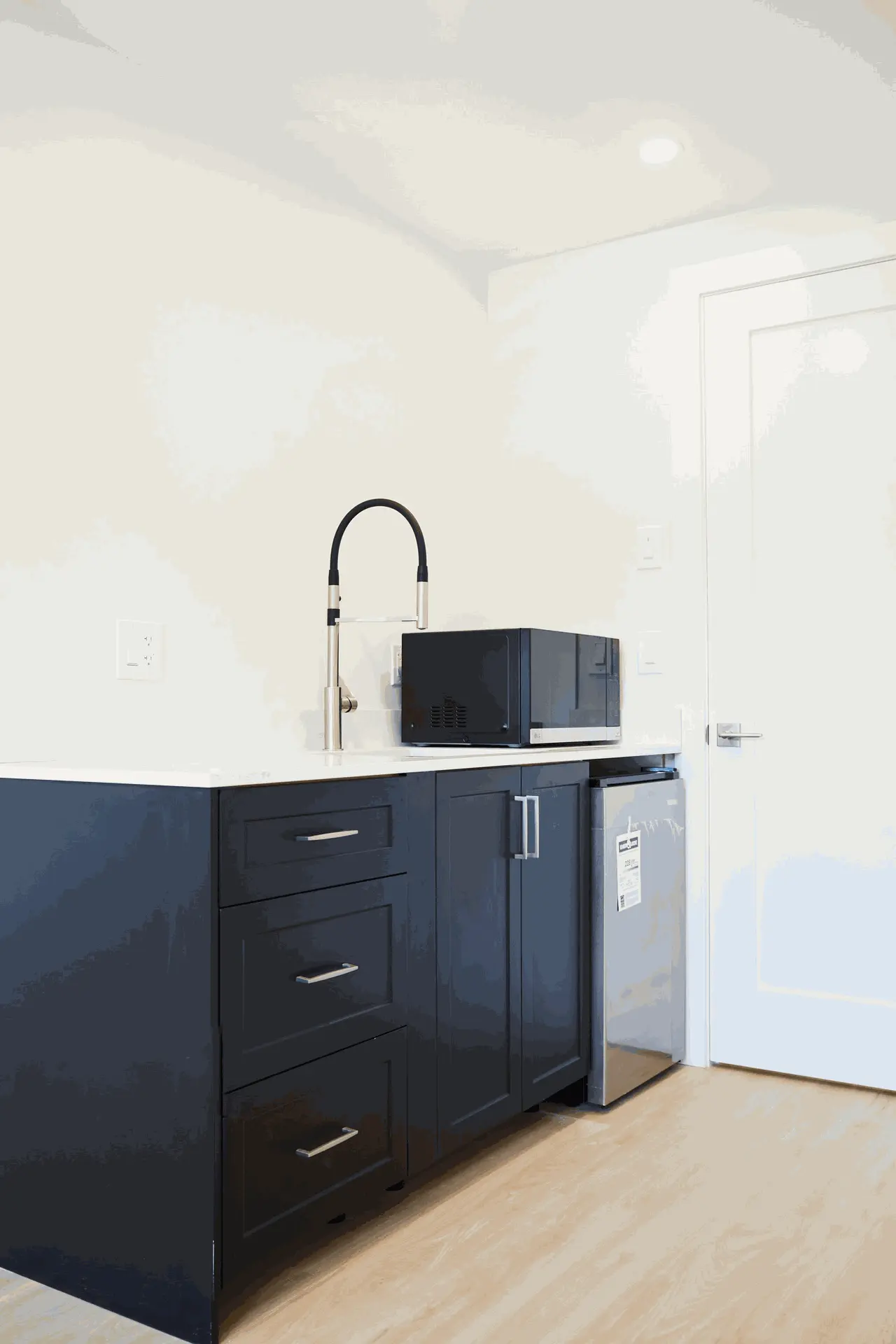 Compact kitchen area featuring dark cabinetry, a modern faucet, a microwave, and a small refrigerator.