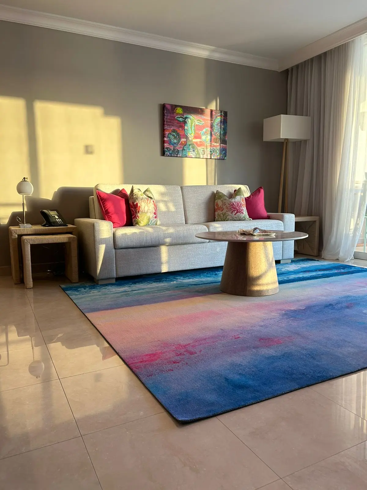 Stylish living area with a cozy sofa, vibrant cushions, and a colorful area rug, illuminated by soft sunset light.