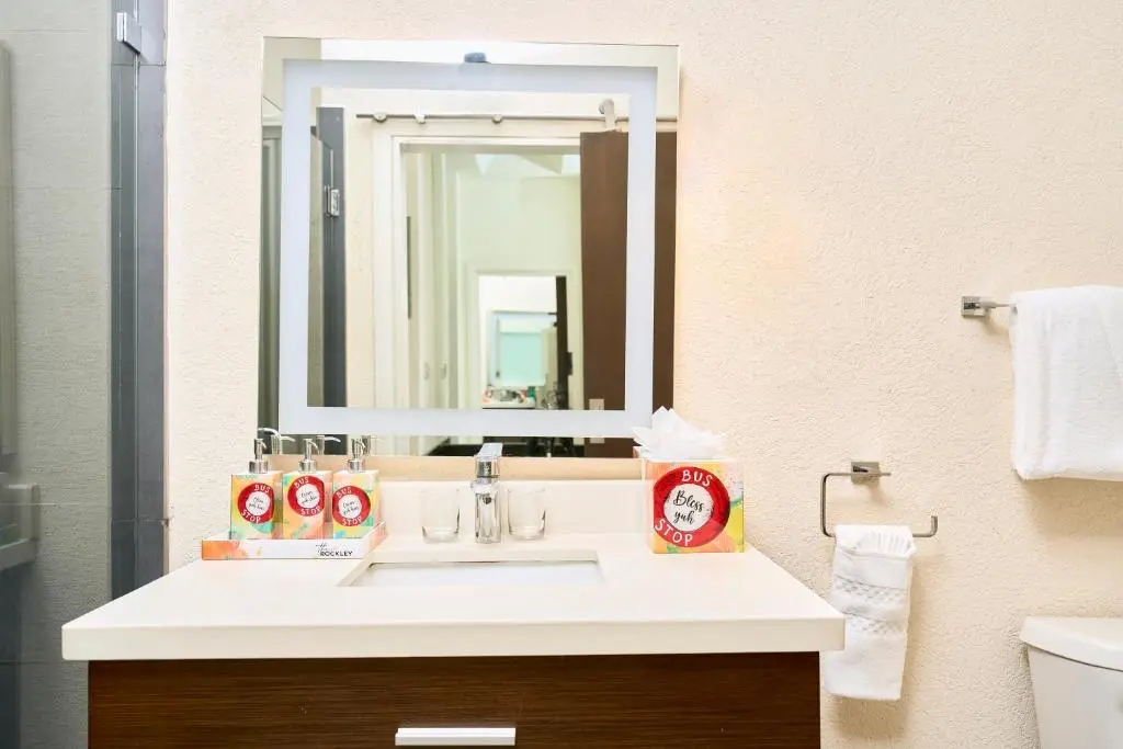 Modern bathroom vanity at The Rockley featuring a sleek sink, stylish mirror, and complimentary toiletries in vibrant packaging.