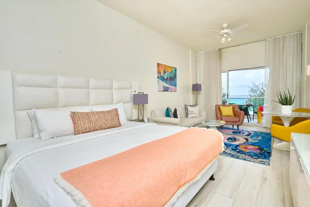 Bright and inviting bedroom at The Rockley, featuring a comfortable king-size bed, modern decor, and a view of the sea through large windows.