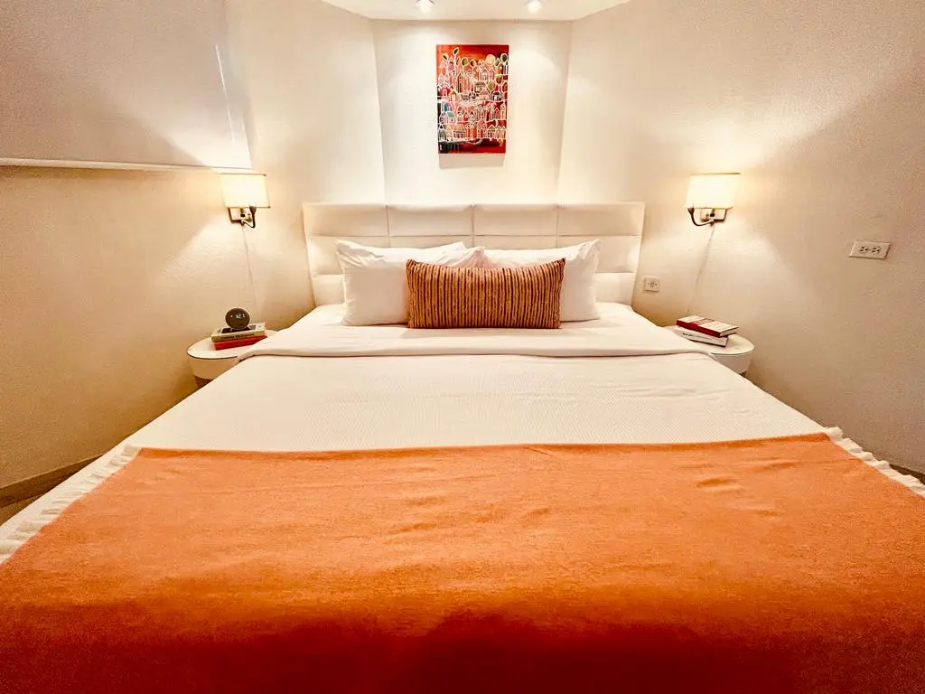 Cozy bedroom at The Rockley featuring a plush bed with decorative pillows, soft lighting, and a vibrant piece of artwork on the wall.
