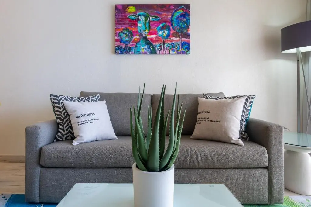 Cozy seating area at The Rockley featuring a gray sofa with decorative pillows, a vibrant artwork above, and an indoor plant for a touch of freshness.