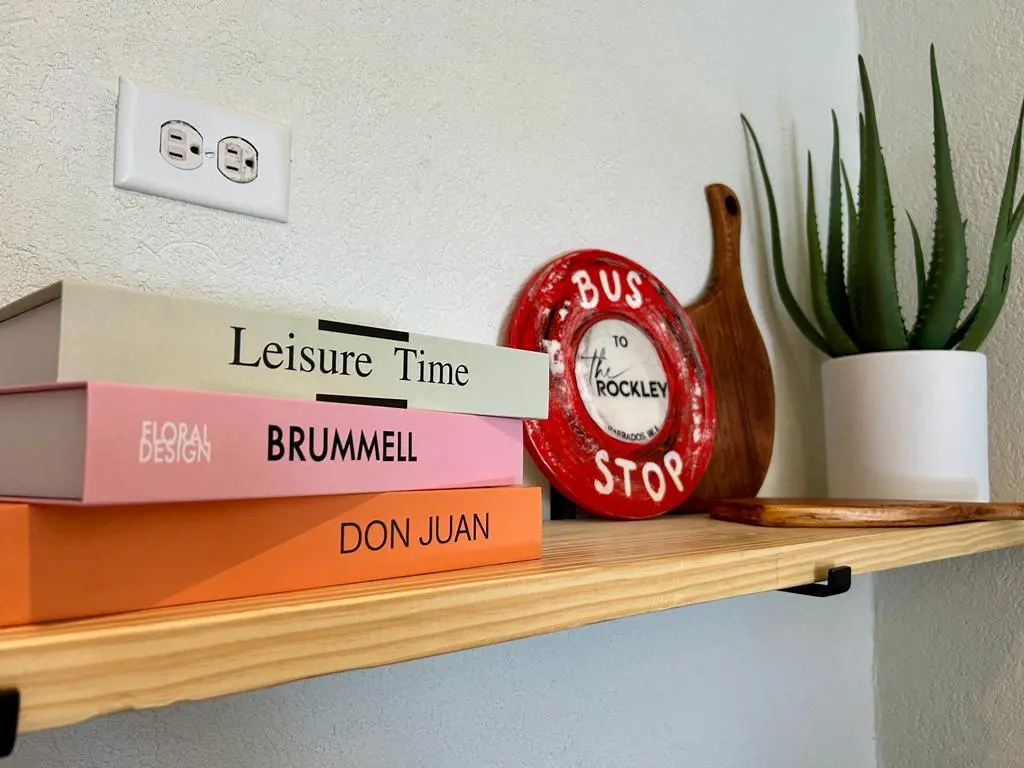 A stylish shelf at The Rockley displaying colorful books, a decorative plate, a wooden cutting board, and a potted plant.