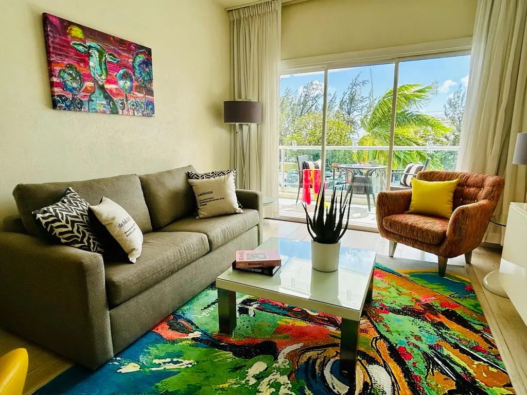 Lively living room at The Rockley featuring a comfortable sofa, colorful artwork, and large windows that provide a bright view of the outdoor seating area.