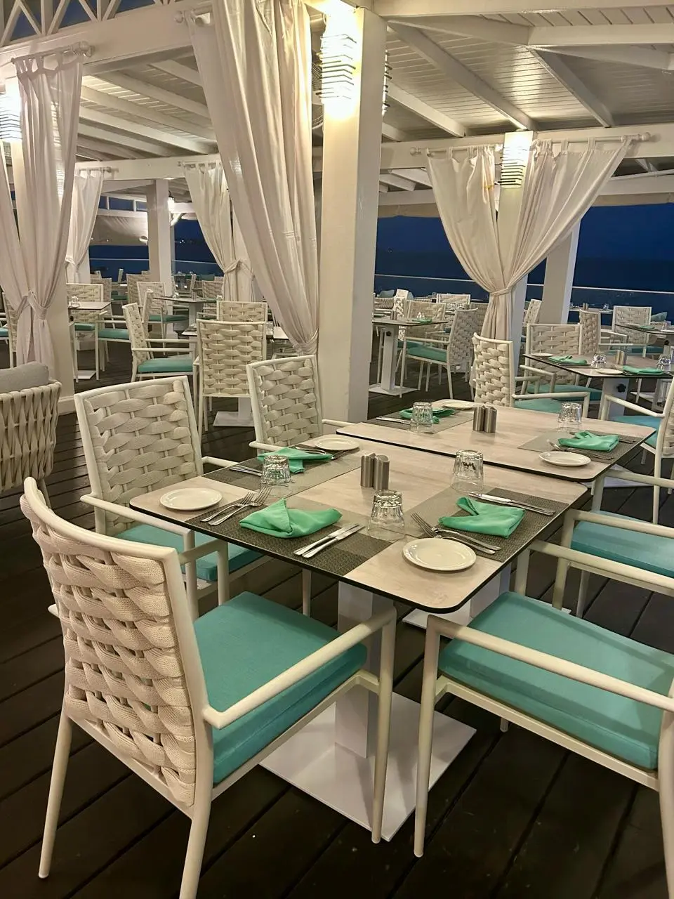 eautifully arranged dining tables at Aqua Terra Restaurant, featuring white wicker chairs with turquoise cushions and a serene coastal view.