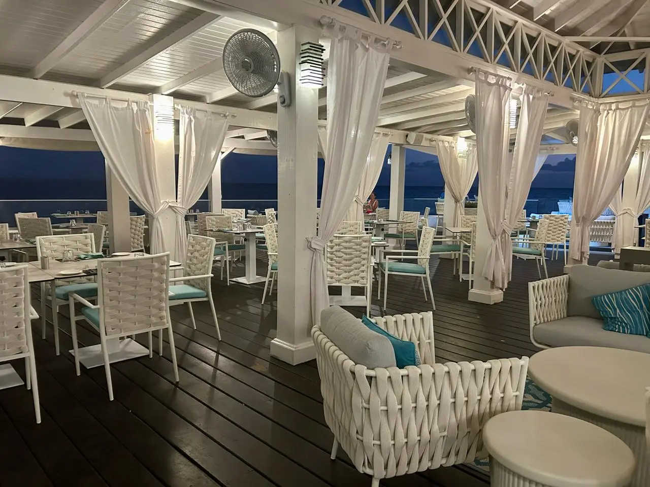 Elegant outdoor dining space at Aqua Terra Restaurant featuring white wicker furniture, soft drapes,