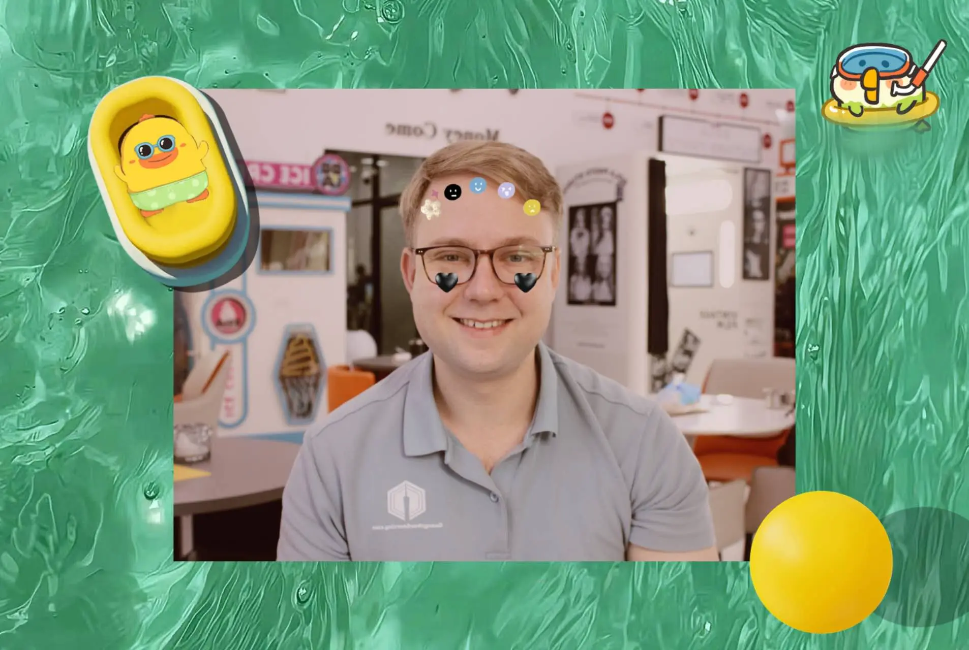 A smiling person wearing glasses posing in a photo booth with playful overlays and stickers on the face;