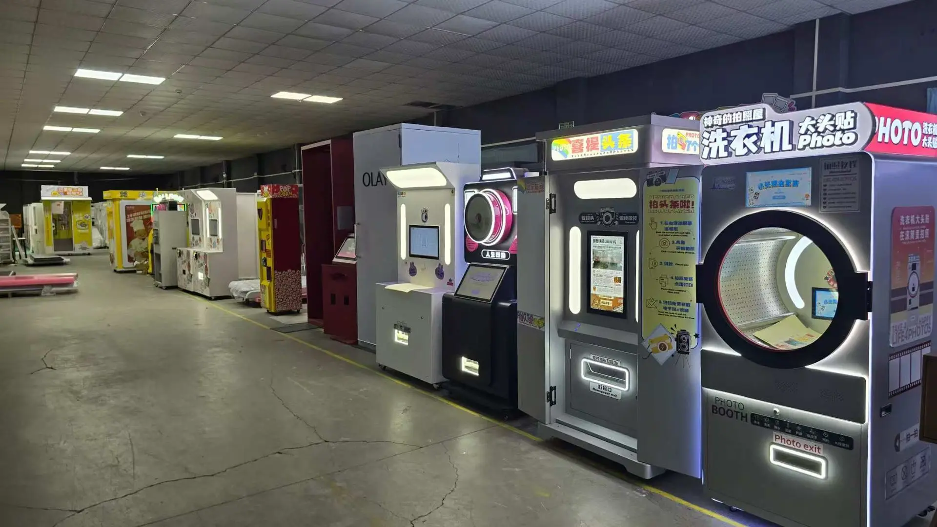 A row of photo booths and vending machines lines the wall of a dimly lit indoor space with a cracked concrete floor.