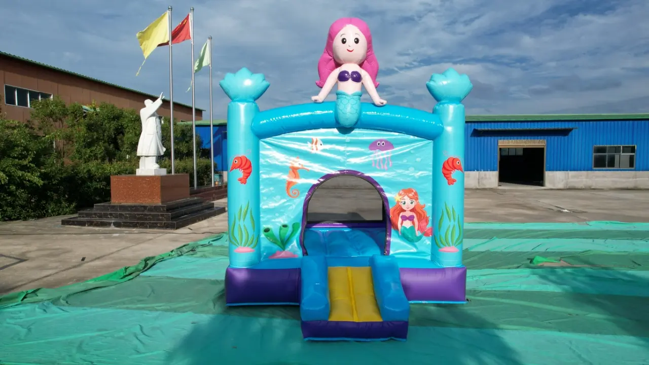 Mermaid Theme Inflatable Bounce House with Tower Toppe Colorful inflatable bounce house with a mermaid theme featuring a pink mermaid on top, turquoise arches, sea-themed wall graphics, and a small blue-and-yellow ramp at the fron