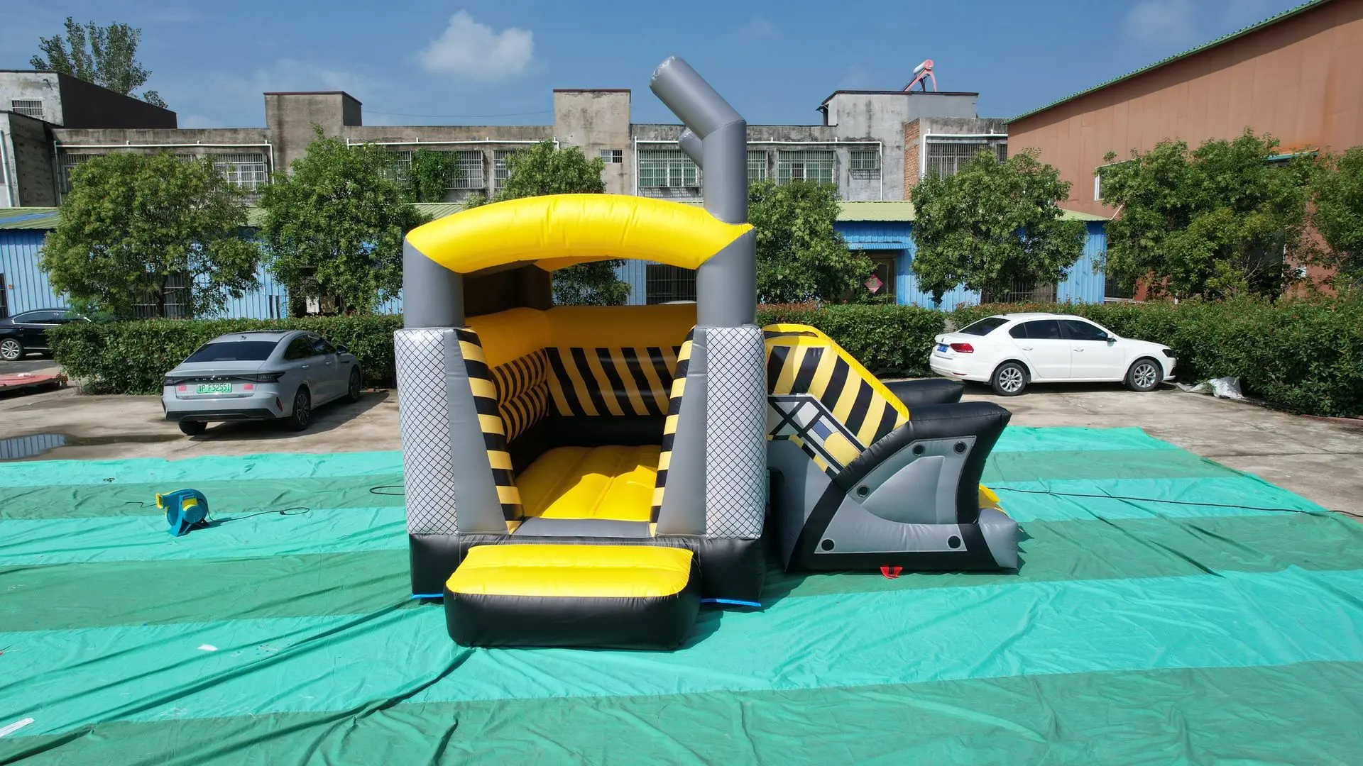 Inflatable Obstacle Course with Slide - Yellow, Gray, and Black Details on Outdoor Setup A yellow and gray inflatable obstacle course with a small splash pool at the front, black-and-yellow striped sides, an inflated arch at the top, and a gray slide/platform on the right, set up outdoors