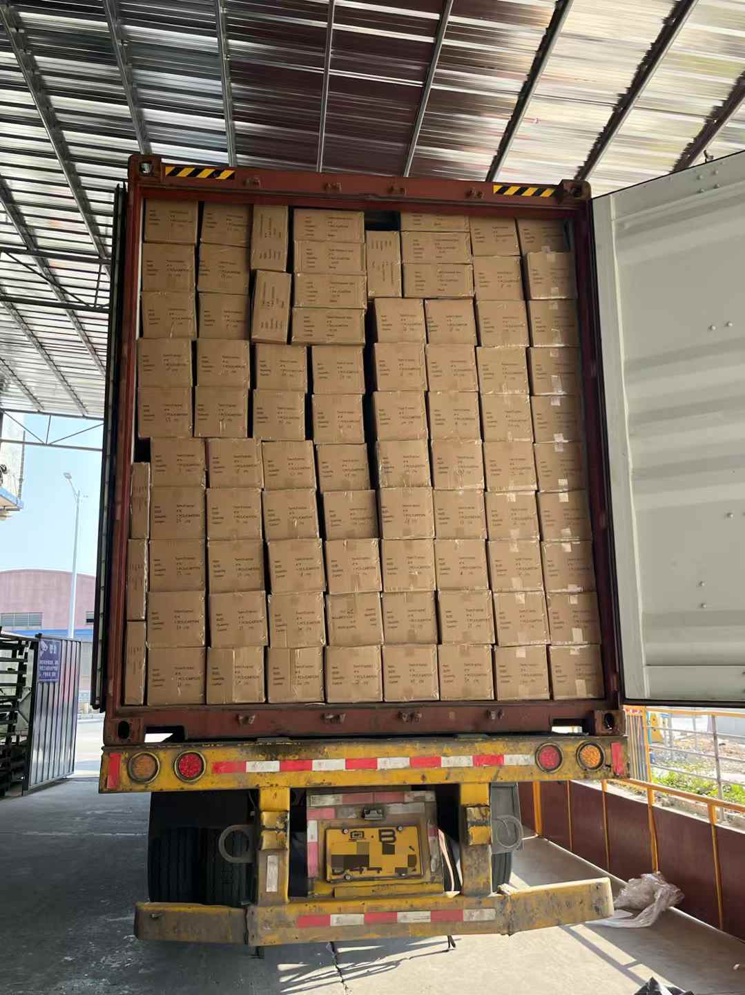 Guangzhou Sourcing shipping container with stacked boxes ready for shipment A shipping container packed full with uniform cardboard boxes, viewed from the rear loading area of a warehouse.
