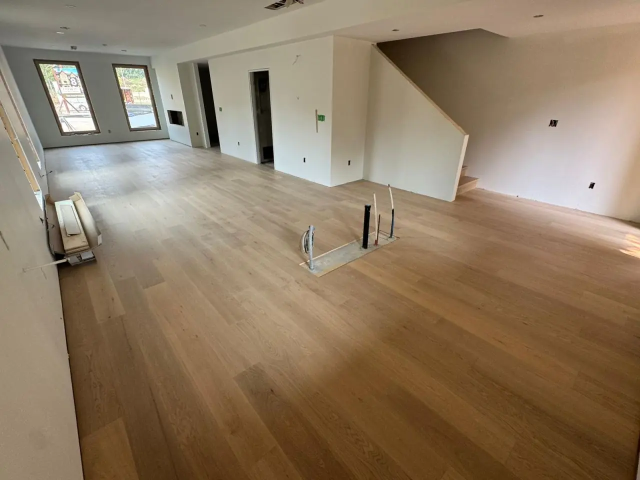 Living area with new timber flooring under construction, open layout, staircase, large windows, and unfinished outlets