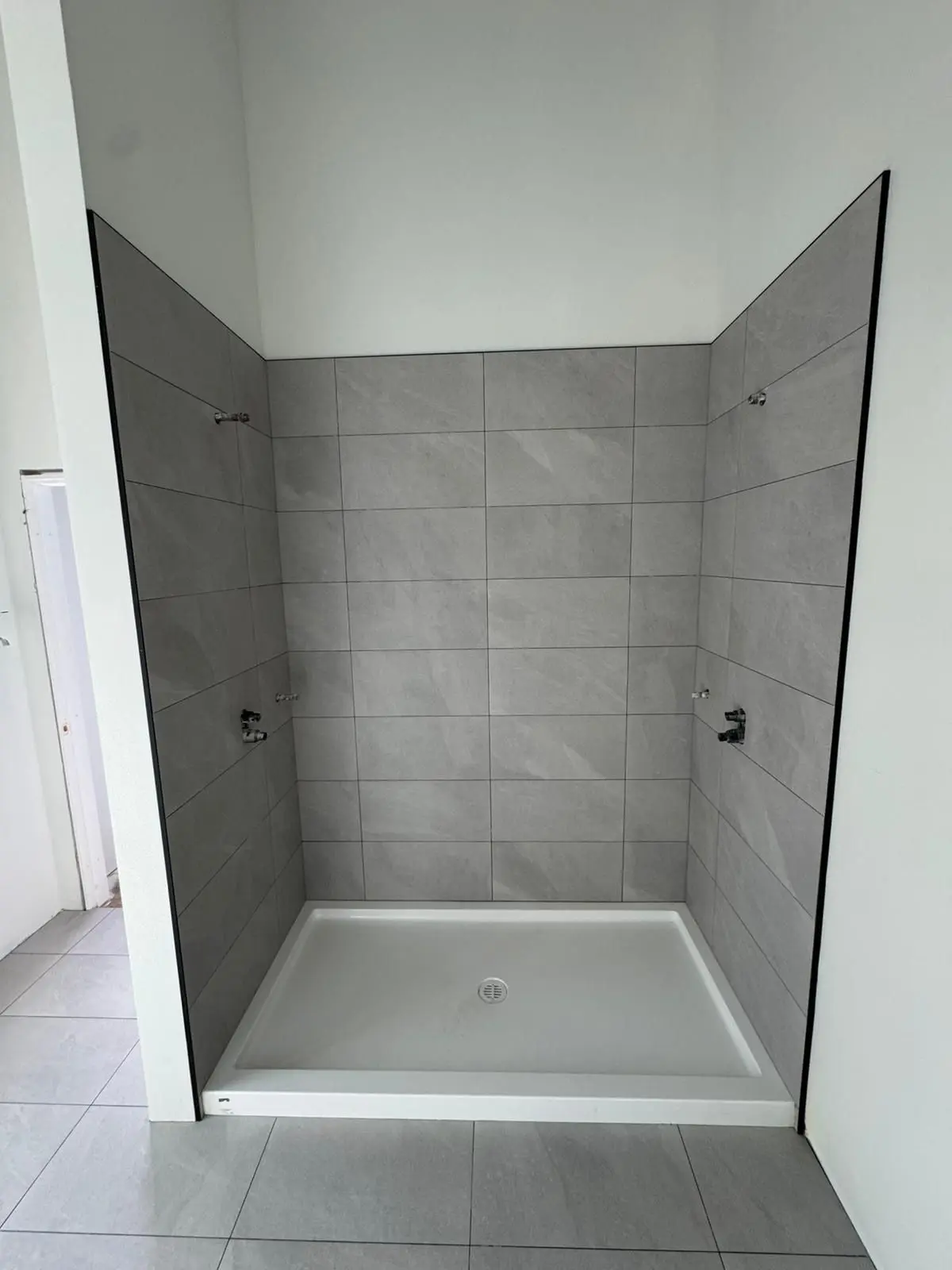 Modern indoor shower area with light gray wall and floor tiles, 