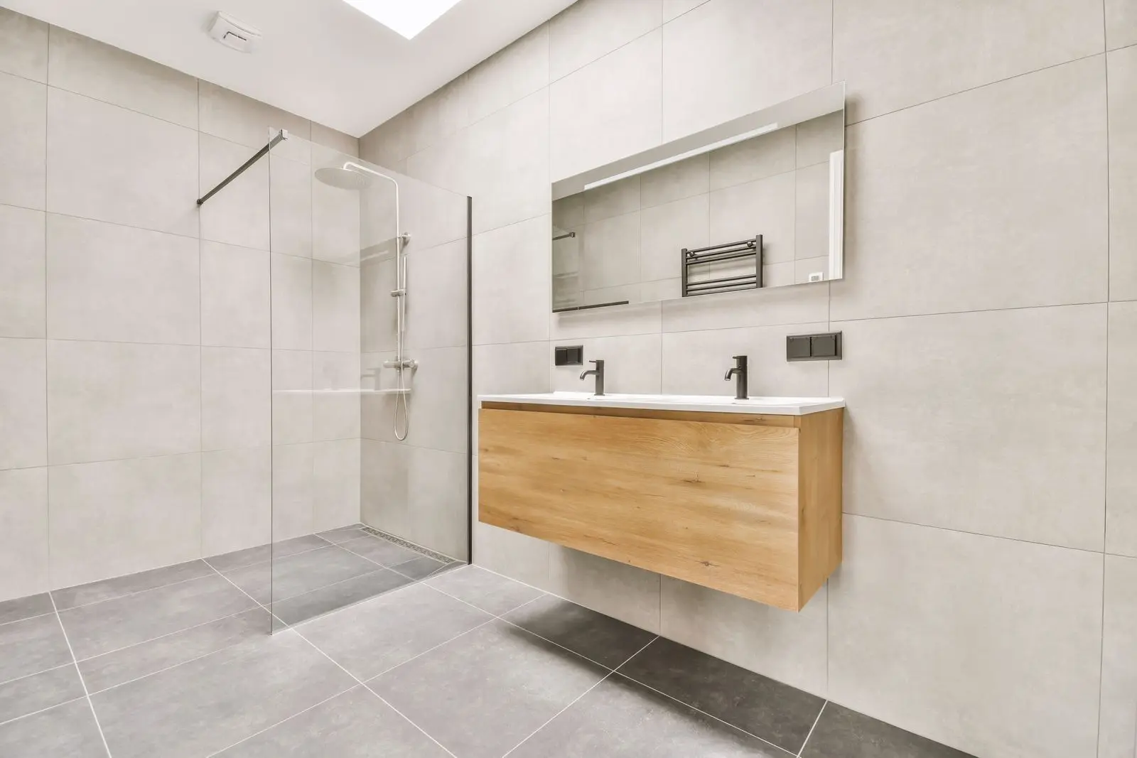 Modern Bathroom Design with Light Gray Tiles and Floating Wood Vanity Modern minimalist bathroom with large light-gray wall tiles, a glass walk-in shower, a floating light-wood double vanity, and a rectangular backlit mirror.