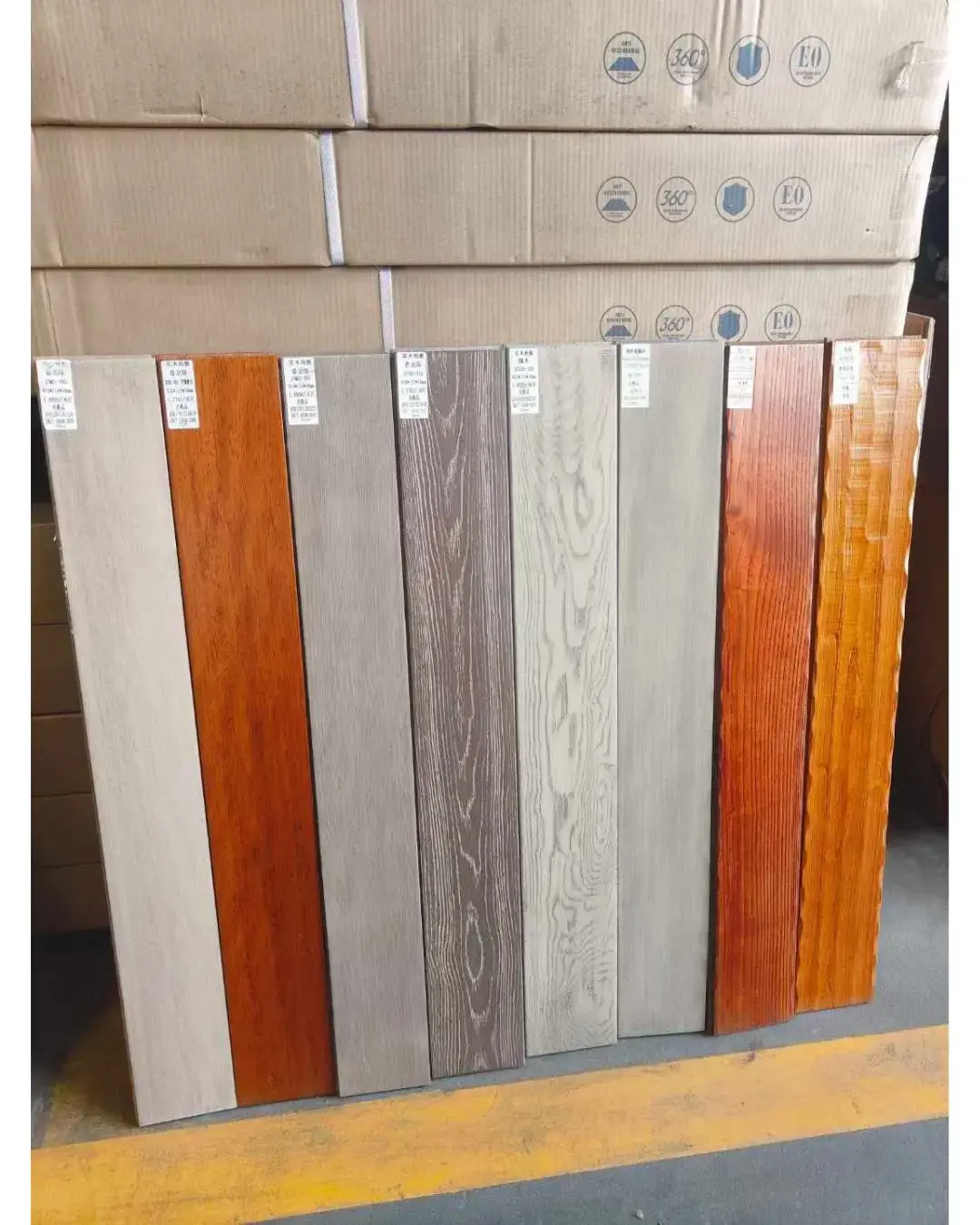 Variety of Tones and Timber Grain Patterns Collection of eight vertical wood-look tile samples arranged in a row, displaying various colors and grain patterns, including light beige, rich reddish-brown, gray-wash, and darker wood tones.