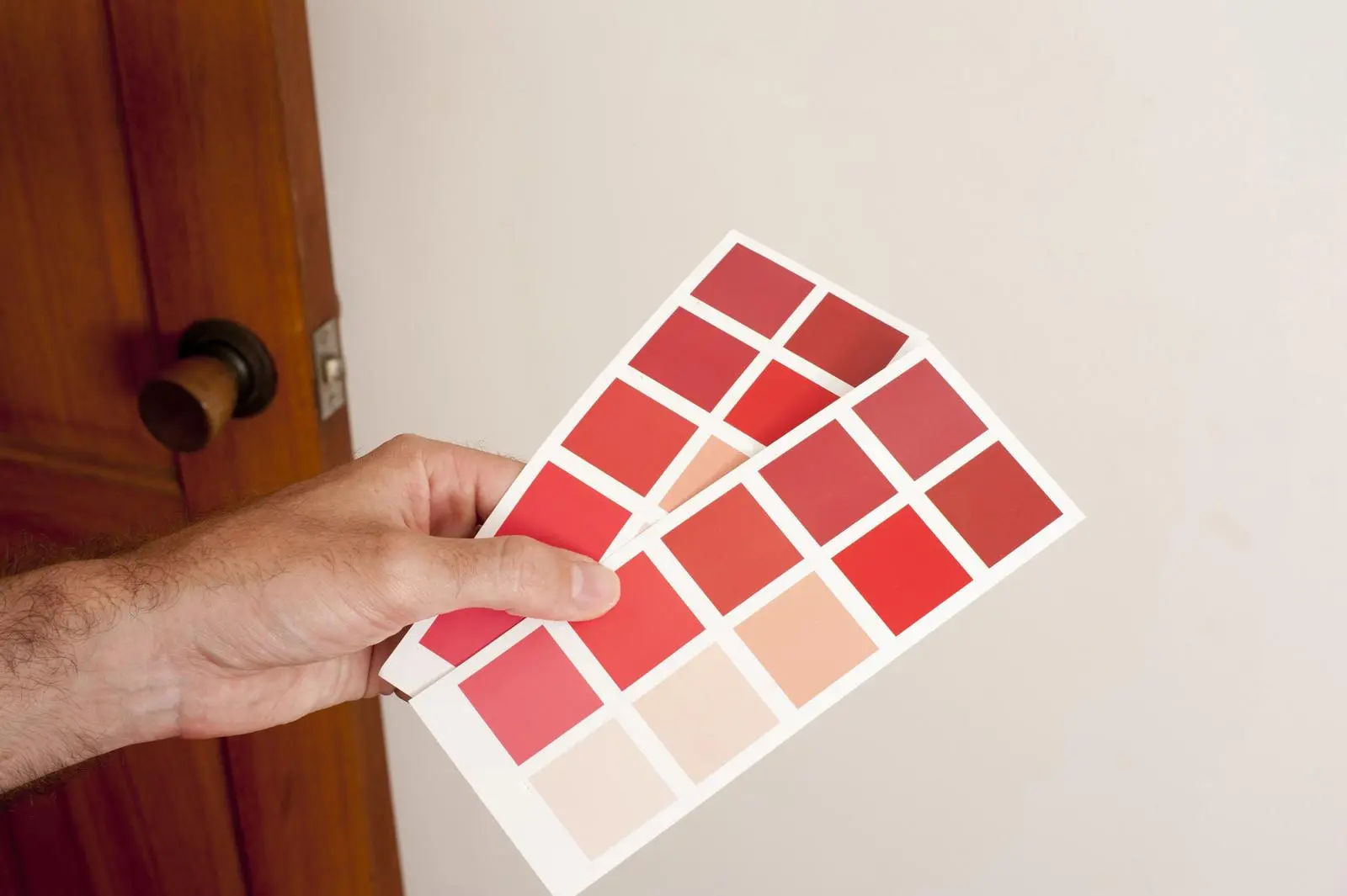Person holding a color swatch card with multiple red and pink shades against a light wall.
