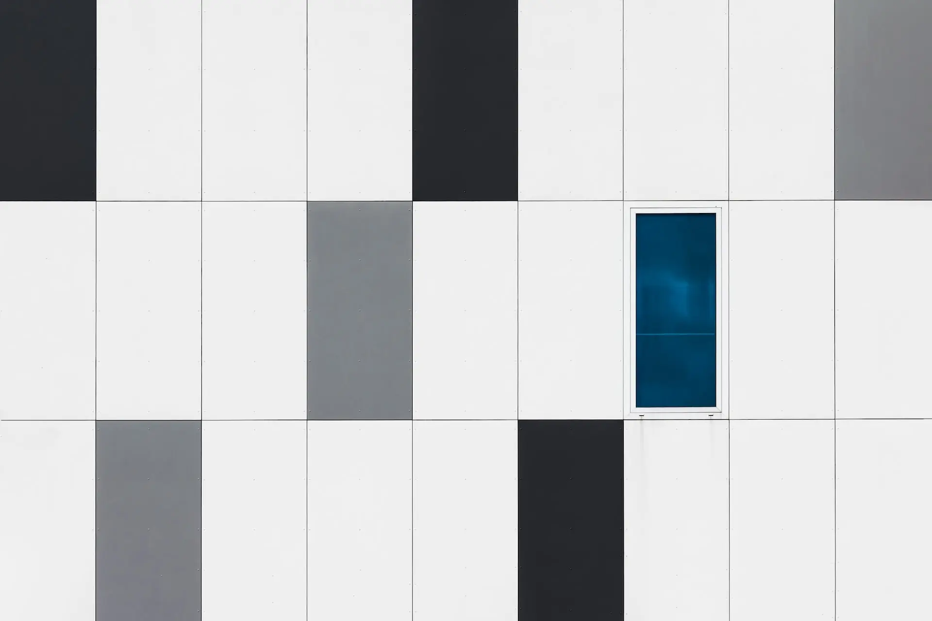 Modern wall tiles in a grid pattern with white, gray, and black tones and a single blue-tinted window section.