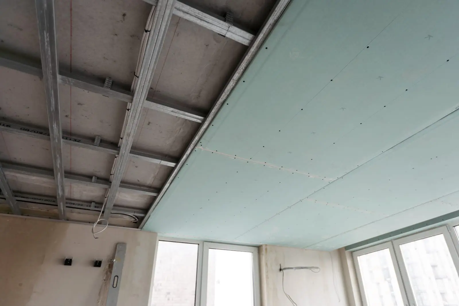 Acoustic Ceiling Systems: Sound Absorption for Offices, Cinemas, and Restaurants Construction site interior showing an unfinished acoustic ceiling with exposed metal framing and light blue gypsum boards, windows, and wires.