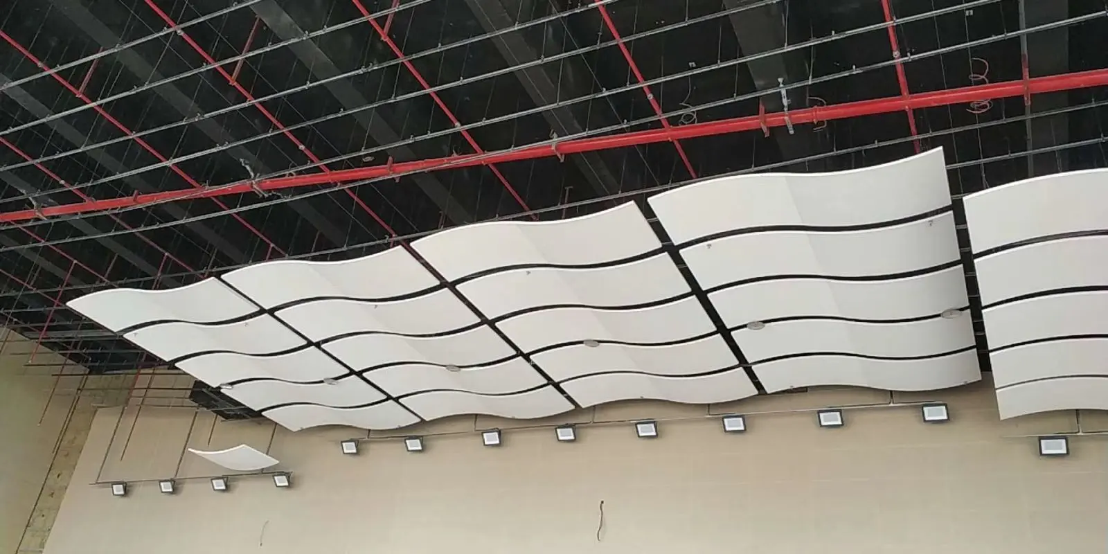 Acoustic Ceiling Production: Installing Wavy White Acoustic Panels Modern acoustic ceiling panels being installed, featuring wavy white panels suspended from an exposed ceiling with red piping.