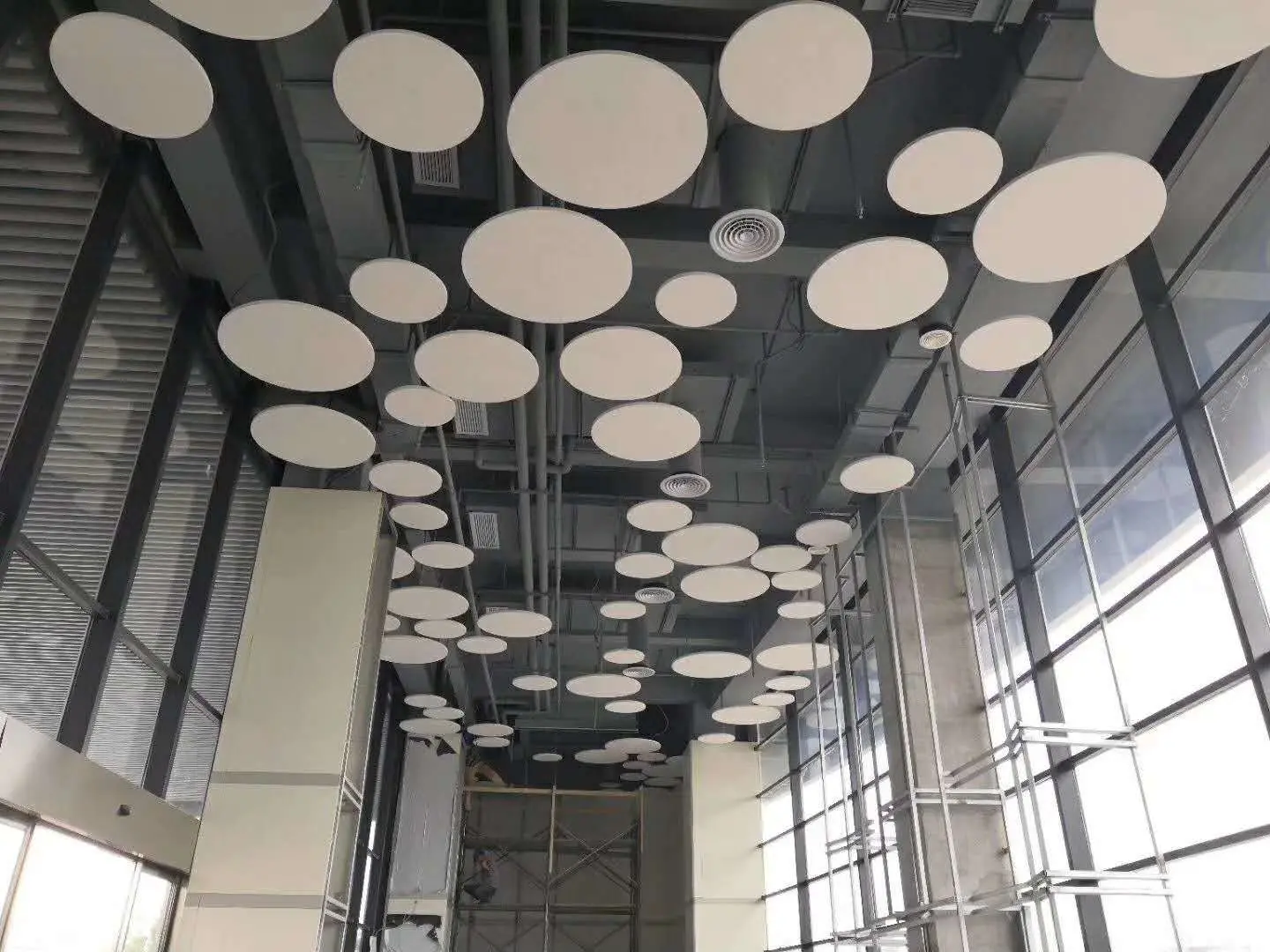 Acoustic Ceiling with Circular Panels: Modern, Quiet Interiors Interior view of a modern office or lobby with a suspended acoustic ceiling featuring numerous white circular panels of varying sizes above glass walls and steel framework.