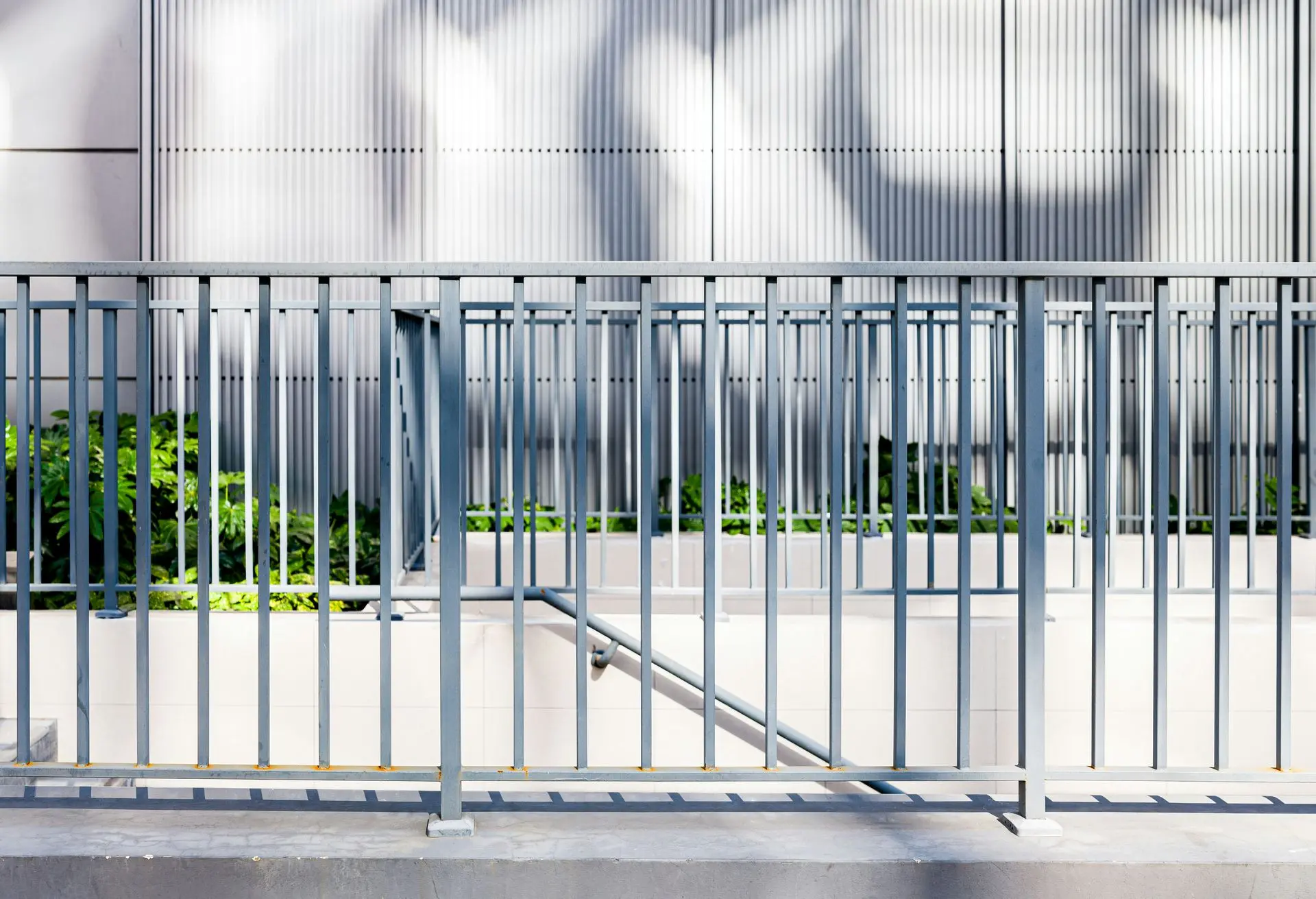 luminum railing with vertical balusters along a modern building facade, casting shadows on the ground.