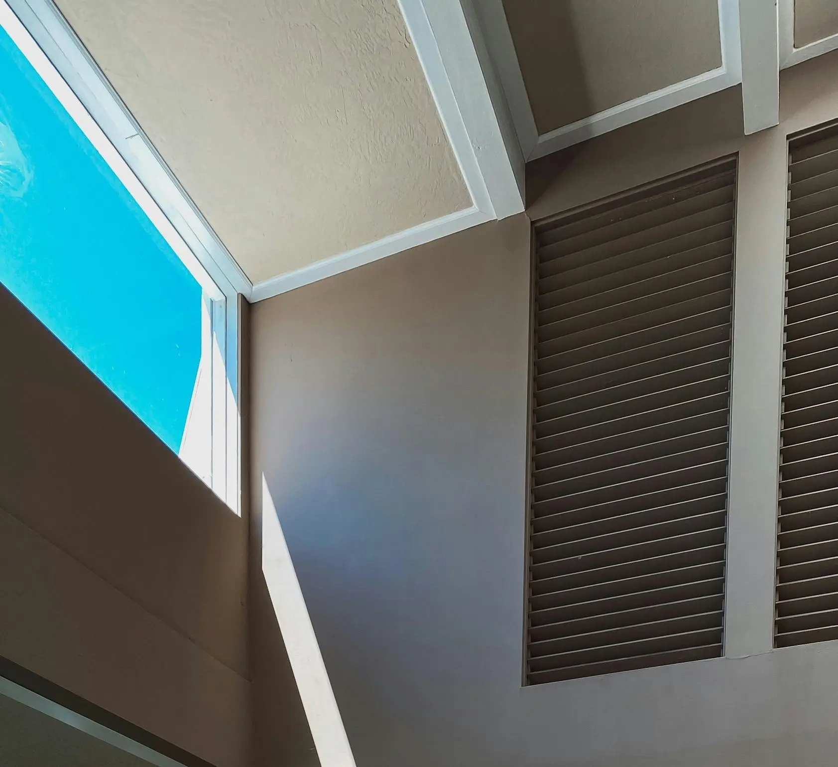Horizontal architectural louvers on a modern building façade “Exterior view of a modern building with dark horizontal architectural louvers set in vertical panels, beige walls, and blue sky visible through a window opening.