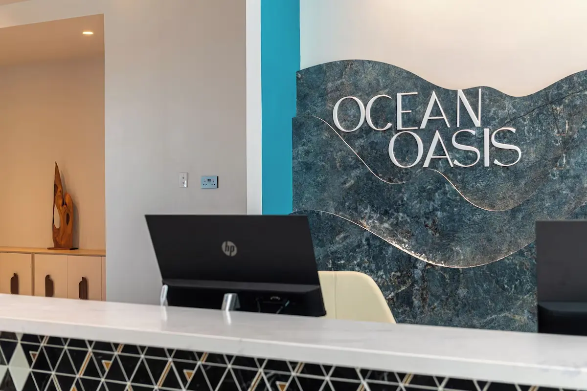 Close-up of the Ocean Oasis Hotel reception desk with a wave-patterned marble backdrop featuring the hotel's logo, showcasing GZS-sourced custom millwork and FF&E.