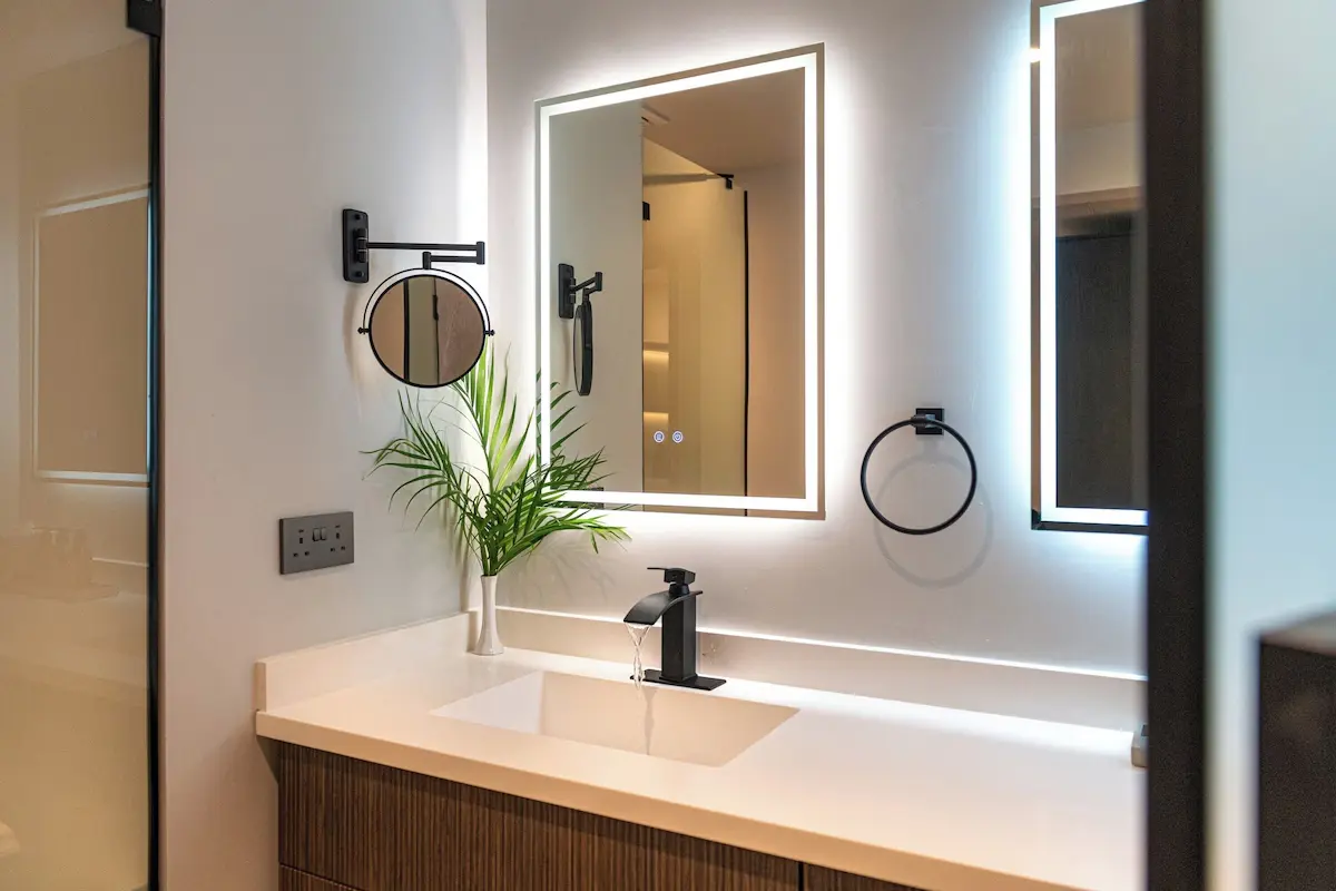 Bathroom Hardware and Mirror - GZS Sourced Items Close-up of a brightly lit bathroom vanity with a single sink, framed mirror, and chrome accessories, highlighting GZS-procured hardware and lighting.