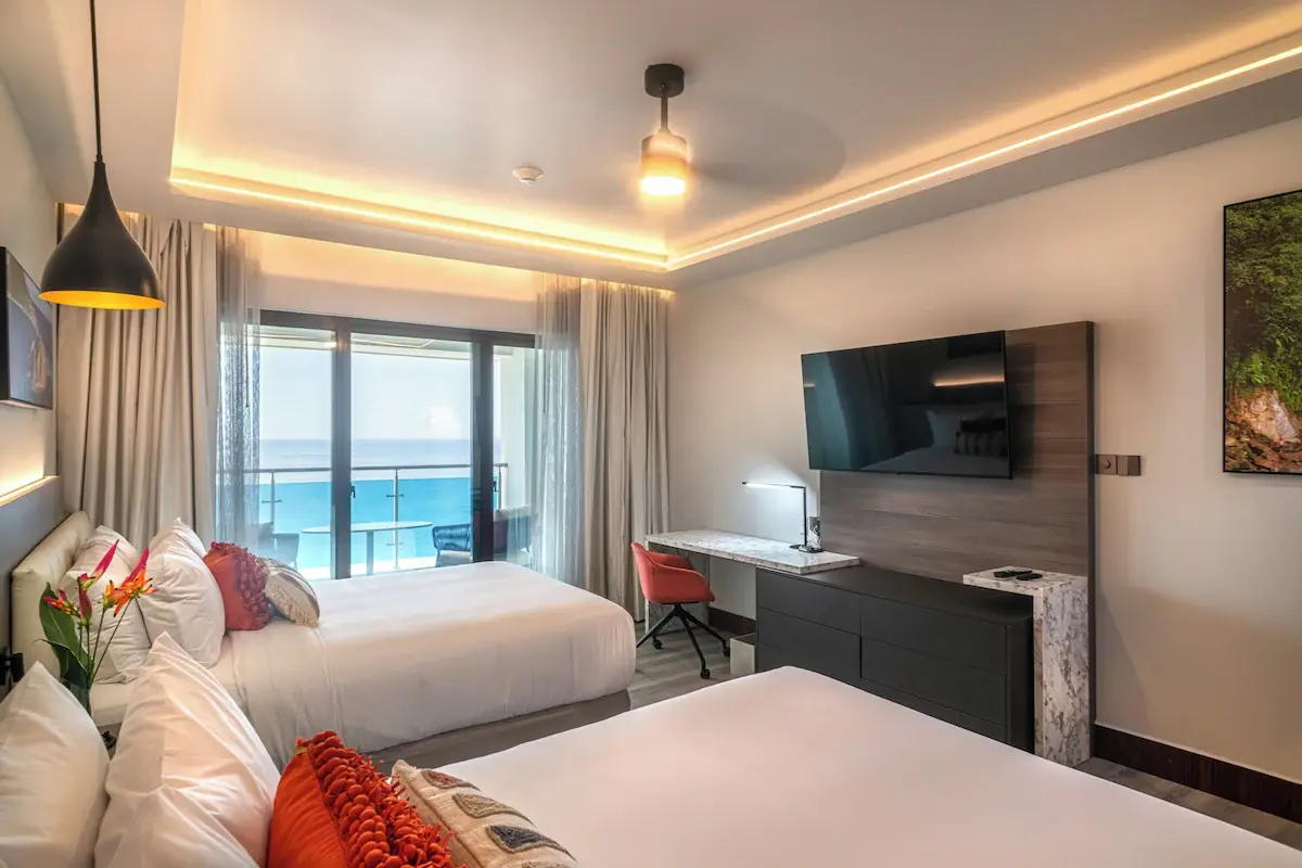 Ocean View Suite - GZS Complete FF&E and Design Ocean Oasis Hotel family suite with two double beds, a desk, a mounted TV, and a balcony view of the coast, reflecting GZS's full FF&E procurement.