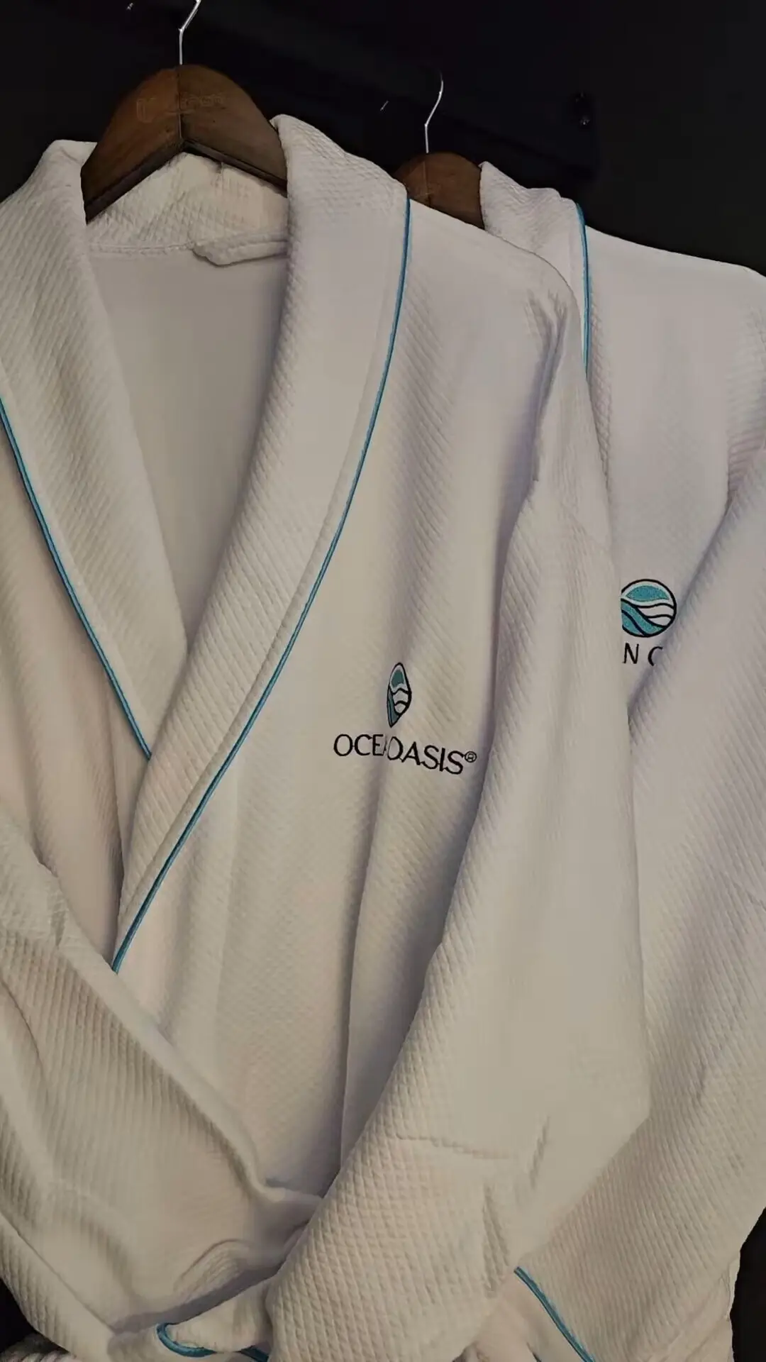 Custom Guest Robes - GZS Sourced OS&E Amenities Two plush white bathrobes embroidered with the "Ocean Oasis" logo hanging on a dark rack, part of the GZS-supplied OS&E (Operating Supplies & Equipment).