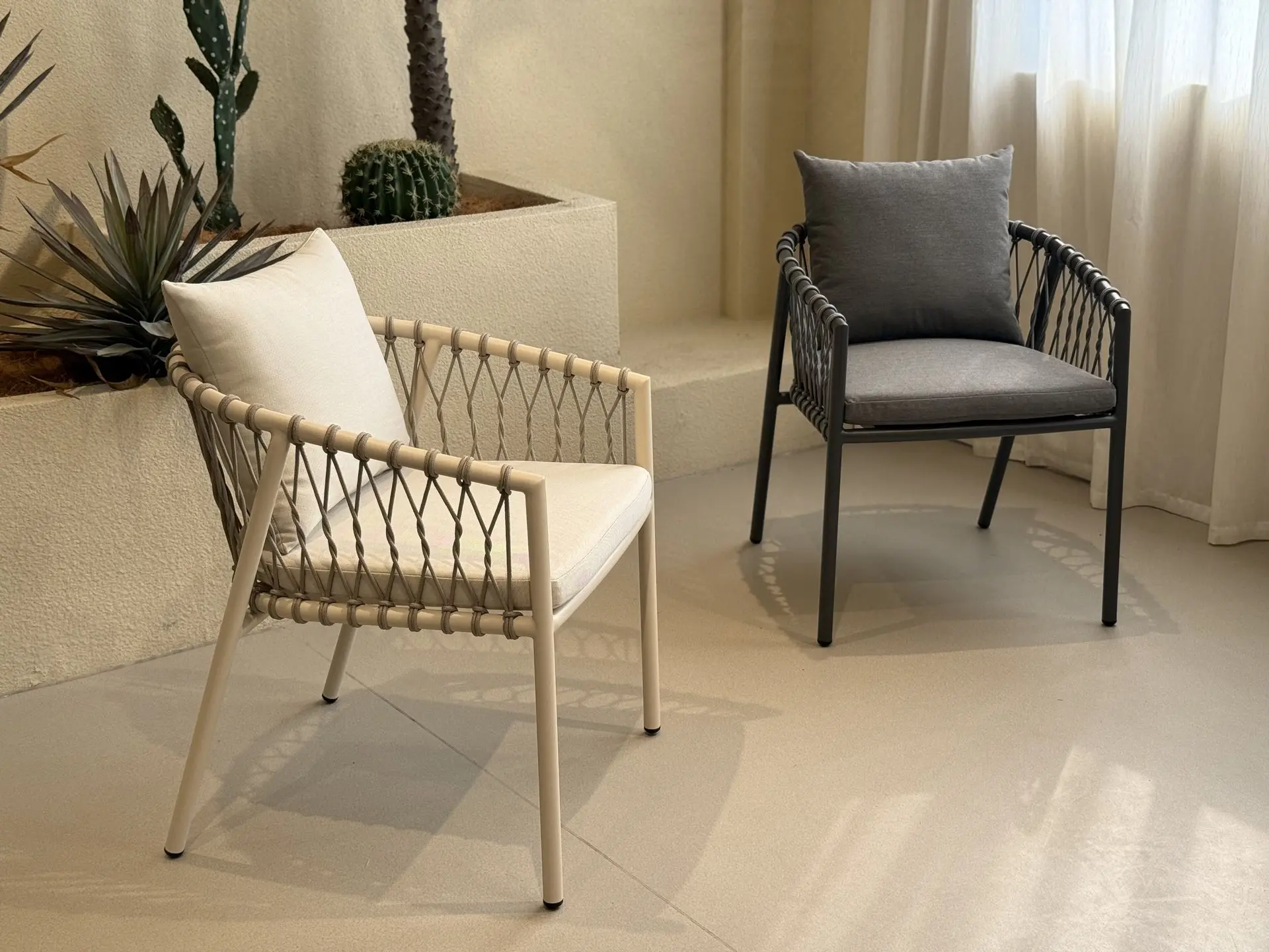 RattanRattan Chair Style Loose Furniture China: Outdoor Woven Seating chair Pair of contemporary outdoor chairs with woven synthetic rattan detailing, used as loose furniture china. One chair is cream with a white cushion, and the other is dark gray with a gray cushion, suitable for patio or garden use.