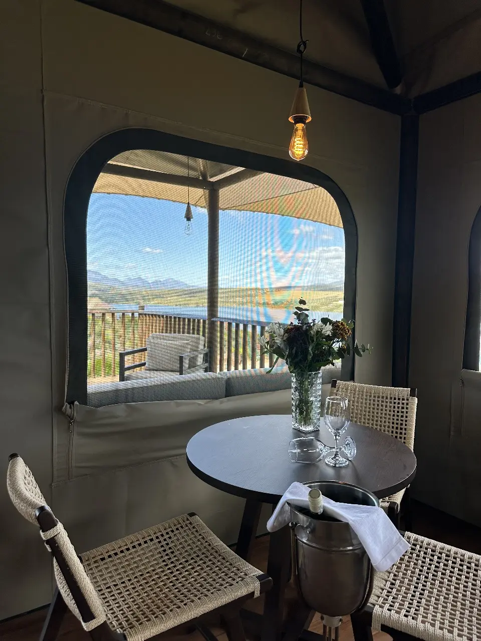 Yamu tent suite dining area with woven chairs, round table, and panoramic window views.