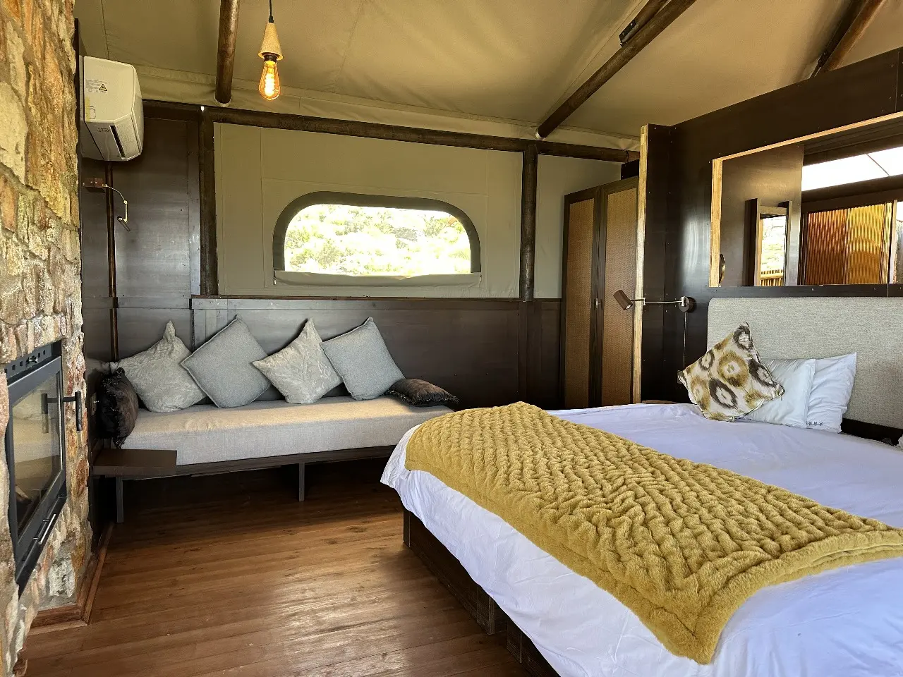 Yamu tent suite bedroom with upholstered bed, soft pillows, wooden flooring, and canvas walls.