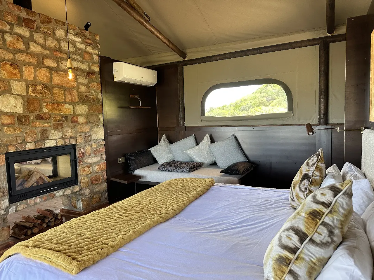 Yamu tent suite bedroom featuring stone fireplace, soft furnishings, and large scenic windows.