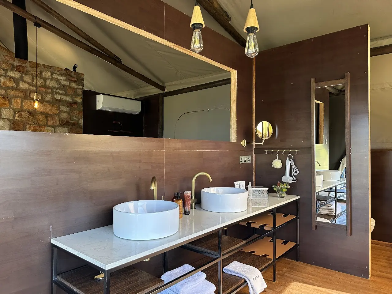 Yamu bathroom vanity with double basins, wood paneling, brass fixtures, and pendant lighting.