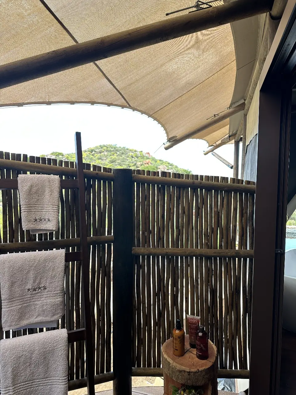 Yamu outdoor shower area with natural reed privacy screen, towels, and rustic wooden accents.