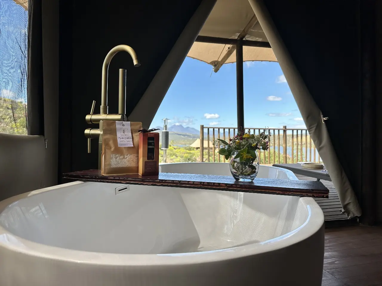 Freestanding bathtub with wooden tray holding amenities and flowers in Yamu tent suite.