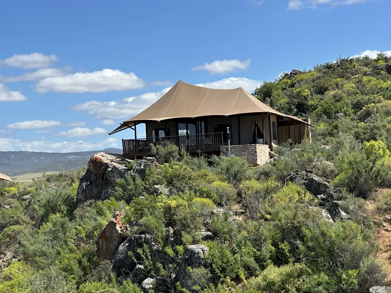 GZS sourced Yamu tent structure with tensile canvas roof and stone base set on a rocky hillside.